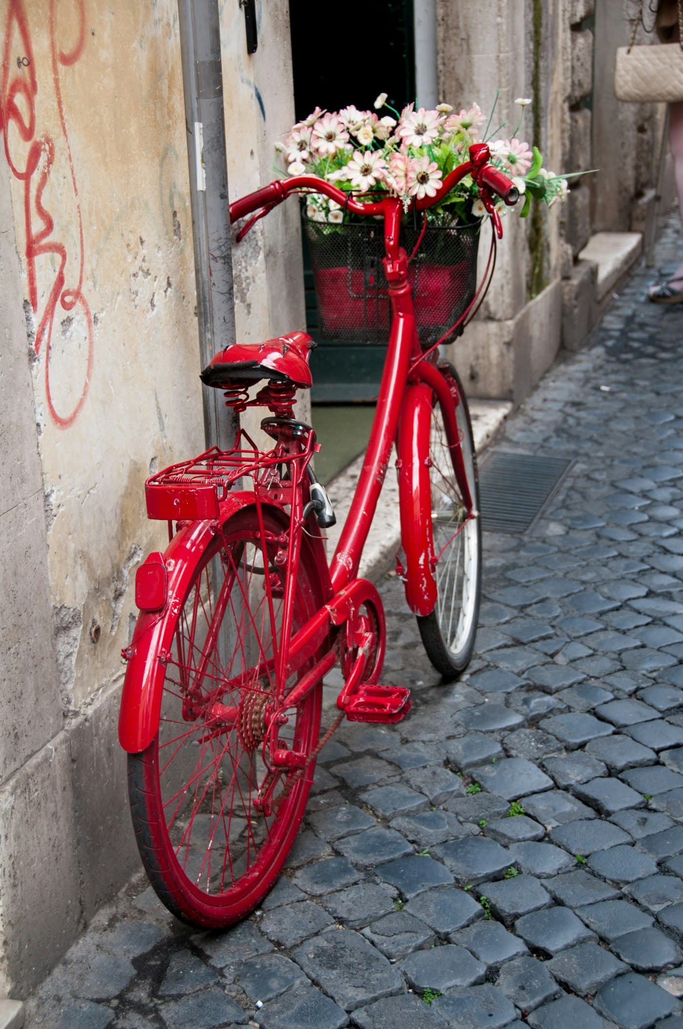Vélo rouge avec un panier fleuri contre un mur de pierre